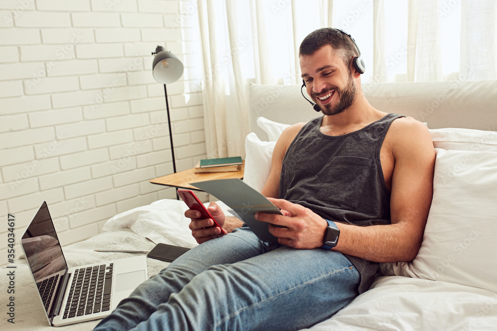 Wall mural Cheerful young man using mobile phone in bedroom