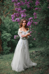 Fototapeta na wymiar portrait of a girl in a white evening dress next to a lilac Bush