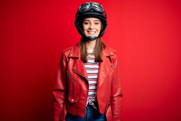Young beautiful brunette motocyclist woman wearing motorcycle helmet and red jacket with a happy...