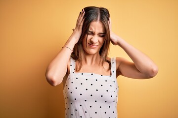 Fototapeta na wymiar Young beautiful brunette woman wearing casual dress standing over yellow background suffering from headache desperate and stressed because pain and migraine. Hands on head.