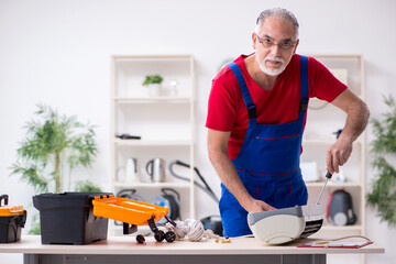 Old male contractor repairing air-conditioner indoors