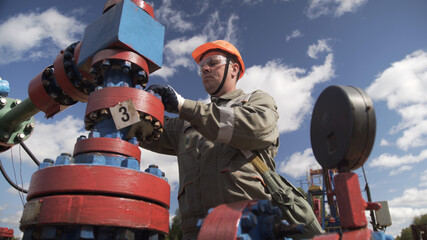 Obraz premium Oilman in orange helmet and protective glass closing valve of x-mass wellhead to shut off well. Decline in oil production after adoption of agreements at meeting of OPEC to stabilize price of oil.