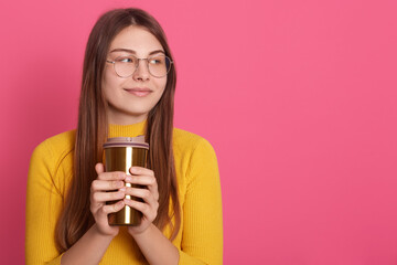 Pensive girl with thermomug in hands, lady looks pensive, looking thoughtfully and smiling aside, enjoying hot beverage. Copy space for advertisement or promotional text.