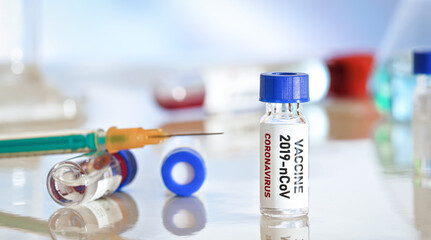 Coronavirus Covid 19 vaccine concept small glass vials with blue caps on white table, green orange syringe near closeup detail