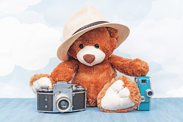 stuffed toy teddy bear in hat sitting and holds old photo camera and retro video camera on a blue...