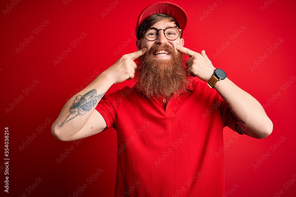 Poster Young handsome delivery man wearing glasses and red cap over isolated background Smiling with open mouth, fingers pointing and forcing cheerful smile