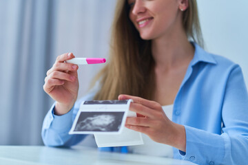 Happy joyful smiling woman looking at a positive pregnancy test result and holding ultrasound image. Planned and long-awaited pregnancy