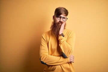 Handsome Irish redhead man with beard wearing glasses over yellow isolated background thinking looking tired and bored with depression problems with crossed arms.