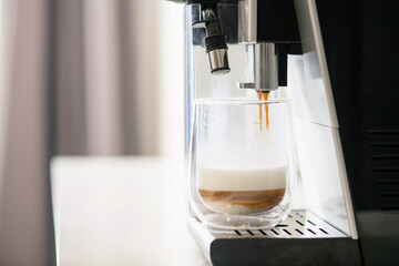 Preparing coffee and milk with machine maker, liquids flow from holder filter to glass transparent cup by layers, automatic making hot beverage at home