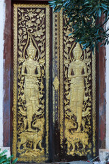 Ancient and artistic wooden entrance door showing relgious buddhst images in Siamese Lao PDR, Southeast Asia