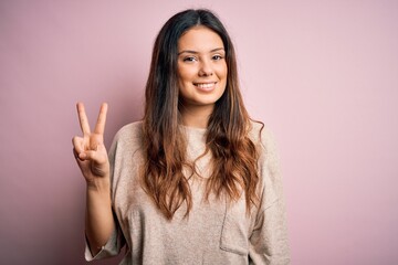 Young beautiful brunette woman wearing casual sweater standing over pink background smiling looking...