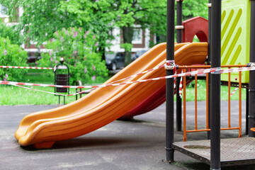 A slide for children to ride on the playground is wrapped with red barrier tape. Prohibition of outdoor walks, prevention of the coronavirus influenza virus covid-19. springtime. selective focus