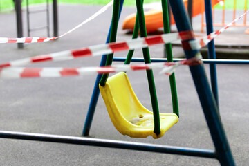 Yellow children's swing in the park wrapped with red barrier tape. Outside. Prohibition of outdoor walks, prevention of the coronavirus influenza virus covid-19. health care. selective focus