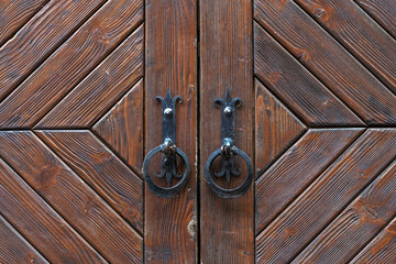 Vintage brown wooden door with two forged handles close up.