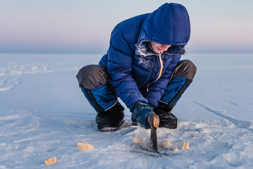 Fototapeta na wymiar Man in blue jacket choping frozen cheese on Baikal Lake. Siberia, Russia
