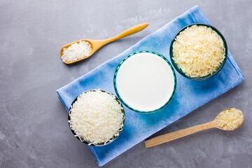 Rice milk and rice seeds on a gray background. Rice milk in glass on a blue napkin. Vegan non-dairy milk on cement background. Alternative milk from rise. Minimalism. Copy space