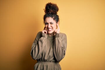 Young beautiful brunette woman with curly hair and piercing wearing casual dress covering ears with fingers with annoyed expression for the noise of loud music. Deaf concept.