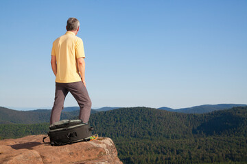 Mature hiker standing on a rock in front of hills with forest