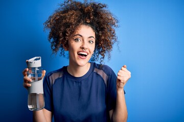 Young beautiful sporty woman with curly hair and piercing doing sport holding bottle of water screaming proud and celebrating victory and success very excited, cheering emotion