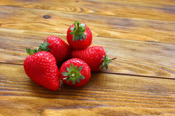 five red ripe strawberries lie on a brown wooden table