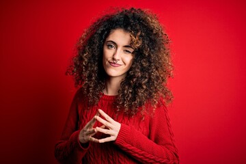 Young beautiful woman with curly hair and piercing wearing casual red sweater Hands together and fingers crossed smiling relaxed and cheerful. Success and optimistic