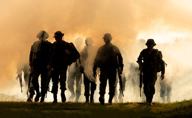 silhouette of unrecognized soldiers with rifle walk through smoke, yellow smoked background. 