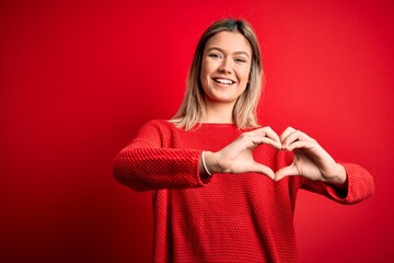 Young beautiful blonde woman wearing casual sweater over red isolated background smiling in love doing heart symbol shape with hands. Romantic concept.