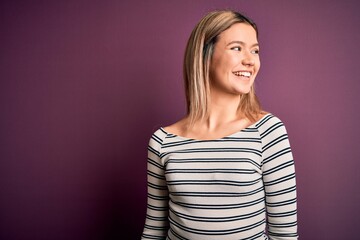 Fototapeta premium Young beautiful blonde woman wearing casual striped shirt over purple isolated background looking away to side with smile on face, natural expression. Laughing confident.