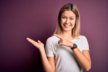 Young beautiful blonde woman wearing casual white t-shirt over purple isolated background amazed and smiling to the camera while presenting with hand and pointing with finger.