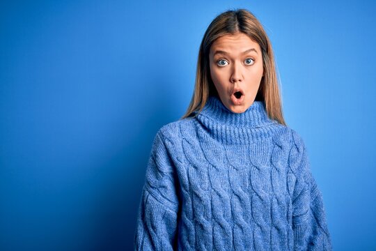 Young beautiful blonde woman wearing winter wool sweater over blue isolated background afraid and shocked with surprise expression, fear and excited face.