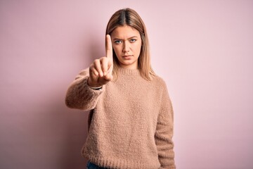 Young beautiful blonde woman wearing winter wool sweater over pink isolated background Pointing with finger up and angry expression, showing no gesture