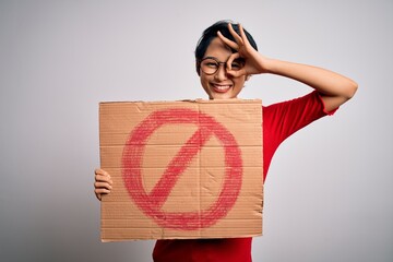 Young beautiful asian girl holding banner with prohibited signal over white background with happy...