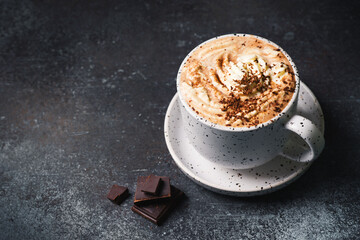 Hot chocolate or cup of coffe with foam and with a piece of chocolate on dark background