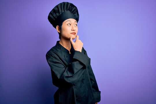 Young beautiful chinese chef woman wearing cooker uniform and hat over purple background Thinking worried about a question, concerned and nervous with hand on chin