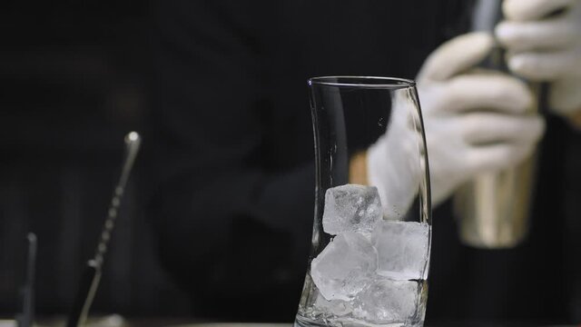 Close up bartenders hands pouring whipped mixture of pina colada coctail into a glass with ice cubes and garnish with whipped cream and pineapple leaves.