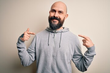 Fototapeta premium Handsome sporty bald man with beard wearing sweatshirt standing over pink background looking confident with smile on face, pointing oneself with fingers proud and happy.