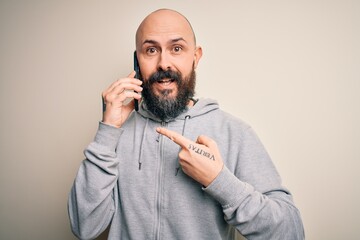 Obraz premium Handsome bald man with beard having conversation talking on the smartphone very happy pointing with hand and finger