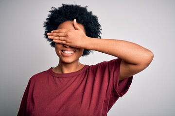 Fototapeta na wymiar Young beautiful African American afro woman with curly hair wearing casual t-shirt standing smiling and laughing with hand on face covering eyes for surprise. Blind concept.