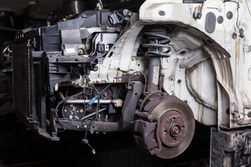 The front of the car after an accident with a disassembled body and metal elements and assemblies under the hood in a car repair shop or garage against a dark background.