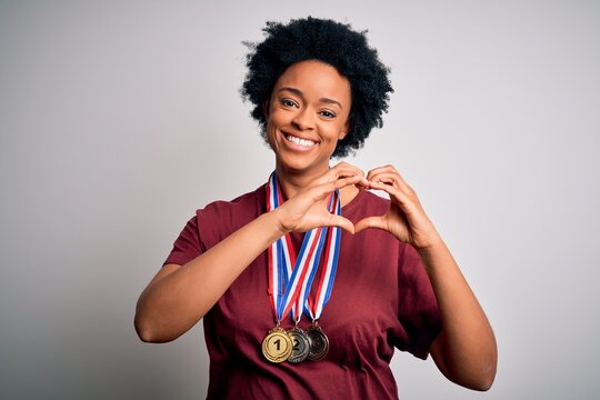 Young African American afro athlete woman with curly hair wearing medals for competition smiling in love showing heart symbol and shape with hands. Romantic concept.