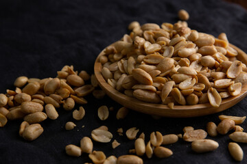 A pile of peanuts in a wooden plate on the black top
