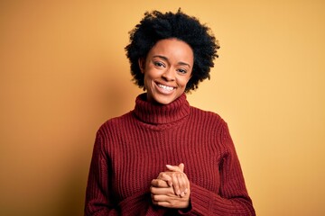 Fototapeta na wymiar Young beautiful African American afro woman with curly hair wearing casual turtleneck sweater with hands together and crossed fingers smiling relaxed and cheerful. Success and optimistic