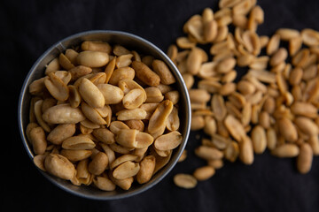 A pile of peanuts in a zinc cup on a black top