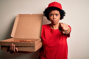 Young African American afro delivery woman with curly hair holding box with Italian pizza pointing with finger to the camera and to you, hand sign, positive and confident gesture from the front