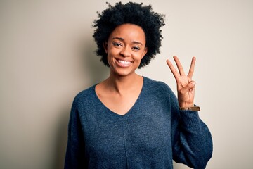 Young beautiful African American afro woman with curly hair wearing casual sweater showing and...