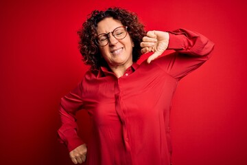 Fototapeta na wymiar Middle age beautiful curly hair woman wearing casual shirt and glasses over red background stretching back, tired and relaxed, sleepy and yawning for early morning