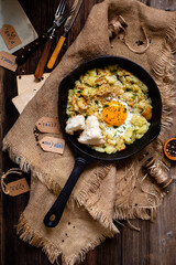 overhead shot of fried potato and egg in cast-iron pan on rustic table with sackcloth
