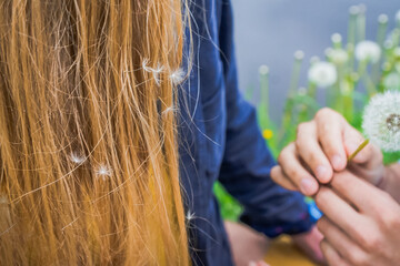 The guy's hands give the girl a dandelion. Dandelion seeds in long blond hair