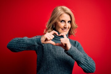 Naklejka premium Middle age beautiful blonde woman wearing casual turtleneck sweater over red background smiling in love showing heart symbol and shape with hands. Romantic concept.