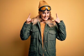 Middle age beautiful blonde skier woman wearing snow sportwear and ski goggles shouting with crazy expression doing rock symbol with hands up. Music star. Heavy music concept.